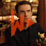 Actor Dan Stevens is sitting at a table in a restaurant looking at someone who is nearer the camera. it's a still image from the movie I'm Your Man (2021)